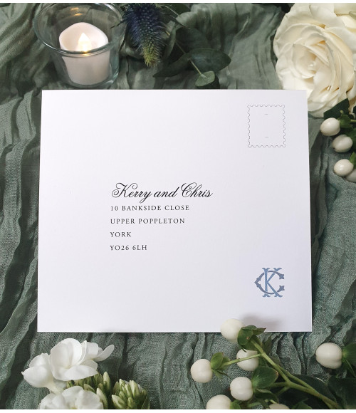 Close-up of dusty blue wedding invitation with monogram initials and pearl card