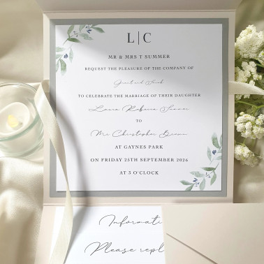 Personalised ivory pocketfold wedding invitation with ivory satin ribbon shown on a luxury flat lay.
