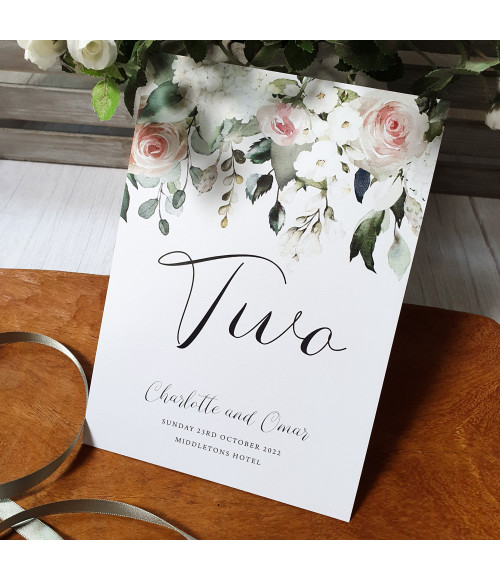 Elegant folded blush rose table name cards on textured card, romantic floral wedding stationery.